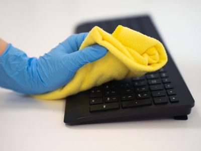 Person cleaning keyboard with a yellow microfiber cloth