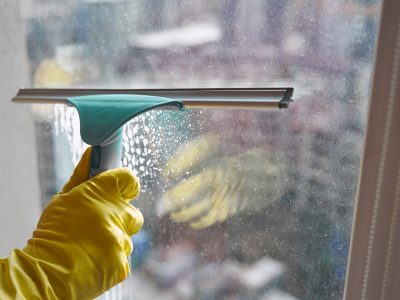 Cropped photo of gloved hand removing cleaning fluid from glass surface with squeegee